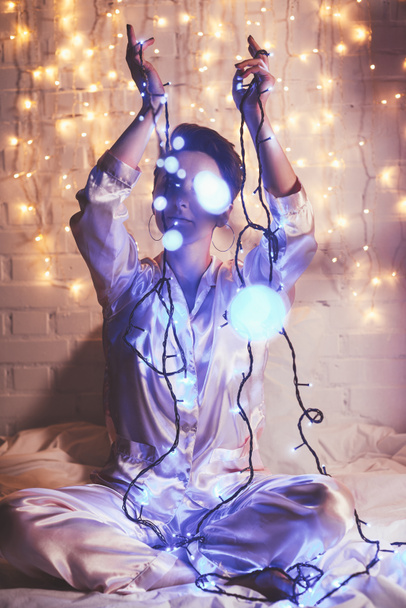 woman in pajamas resting on bed with christmas lights around - Photo, Image