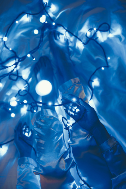 partial view of woman in pajamas on bed with blue festive lights around - Photo, image