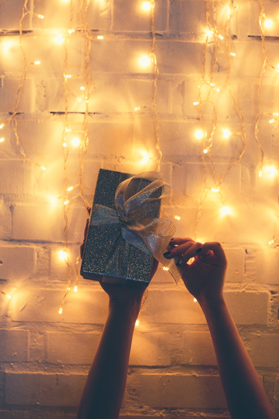 vista parcial de la mujer sosteniendo regalo envuelto con luces de Navidad detrás
 - Foto, imagen