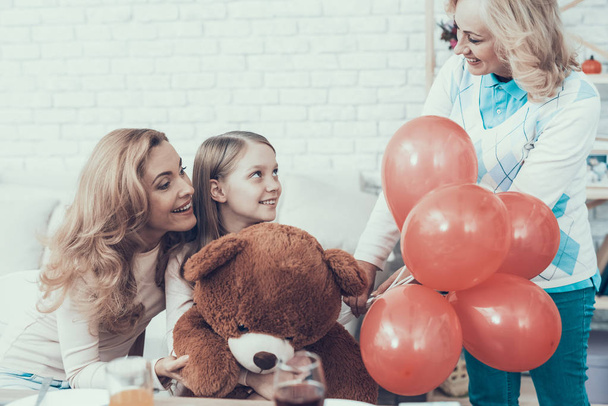Grandmother Giving Toy Bear to Happy Girl at Home. Cake on Table. Happy Family. Mother with Daughter. Smiling Women. Smiling Grandmother. Celebration Concept. Toy Bear. Red Baloons. - Fotografie, Obrázek