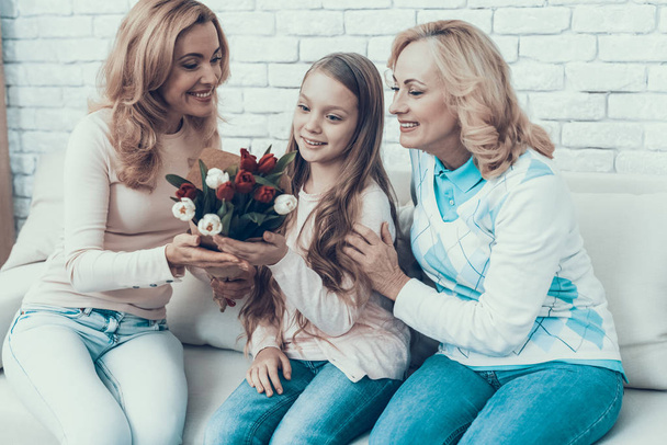 Mother Presents Bouquet of Tulips to Daughter. Mother with Daughter. Smiling Women. Celebration Concept. Happy Family. Sitting at Home. Red Flower. White Flower. Holiday in March. Mother's Day. - Φωτογραφία, εικόνα