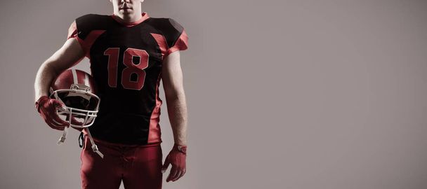American football player standing with helmet against grey background - Foto, Imagen