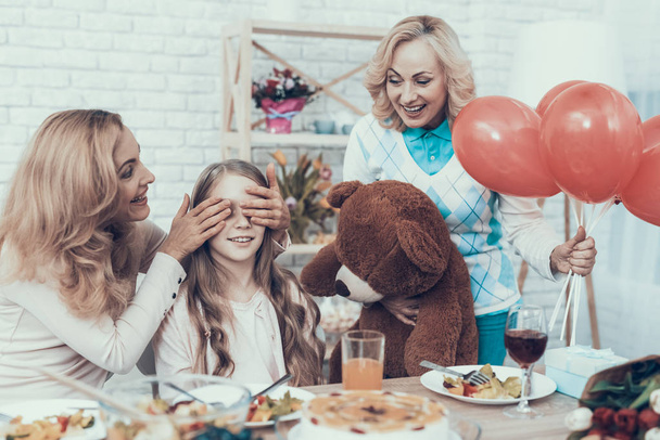 Family Preparing Surprize for Daughter at Home. Cake on Table. Happy Family. Mother with Daughter. Smiling Women. Smiling Grandmother. Celebration Concept. Toy Bear. Closed Eyes. Red Baloons. - Photo, image