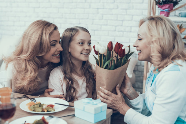Family Celebrating Grandmother's Birthday at Home. Cake on Table. Happy Family. Mother with Daughter. Smiling Women. Smiling Grandmother. Celebration Concept. Glass of Wine. Bouquet of Tulips. - Foto, Imagem