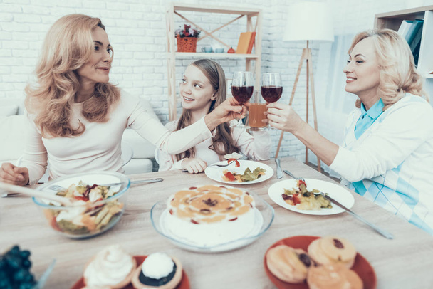 glücklich sitzende Familie feiert Geburtstag zu Hause. Kuchen auf dem Tisch. glückliche Familie. Mutter mit Tochter. Lächelnde Frauen. Lächelnde Großmutter. Festkonzept. Glas Wein. Früchte auf dem Teller. - Foto, Bild