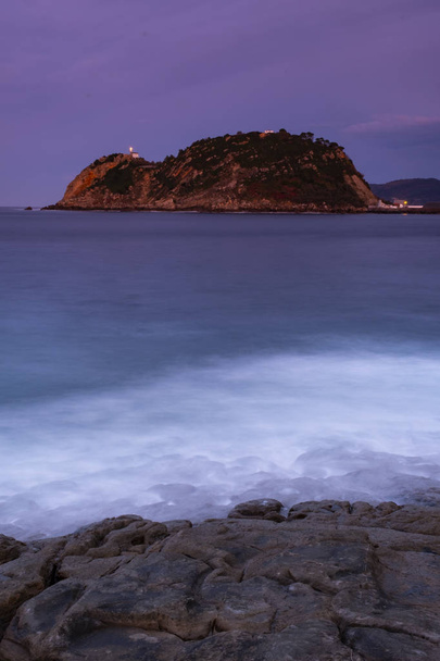 The waves breaking on the rocks at nightfall, with Getaria in the background, Basque Country - Foto, imagen