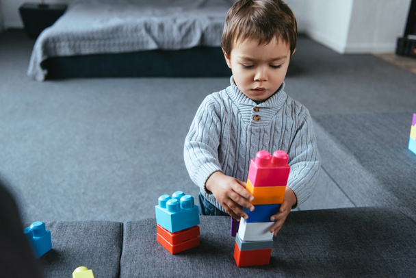 зосереджений маленький хлопчик грає з барвистими пластиковими блоками вдома
 - Фото, зображення