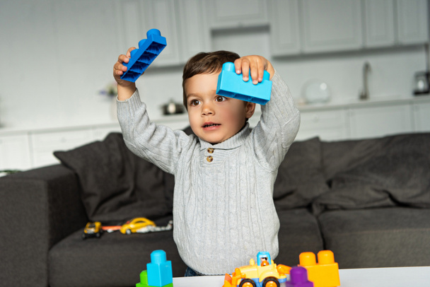 χαρούμενο μικρό αγόρι παίζει με πολύχρωμο πλαστικό μπλοκ στο σπίτι - Φωτογραφία, εικόνα