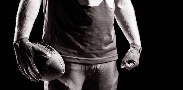 Mid section of American football player standing with rugby ball - Foto, afbeelding