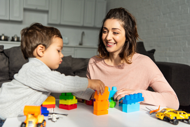 smiling mother and little son playing with colorful plastic blocks at home - Фото, изображение