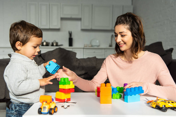 mãe alegre e pequeno filho brincando com blocos de plástico coloridos em casa
 - Foto, Imagem