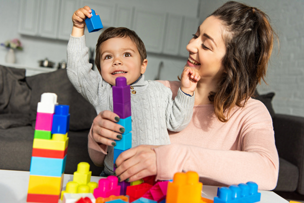 schattige jongen en zijn moeder spelen met kleurrijke kunststof blokken thuis - Foto, afbeelding