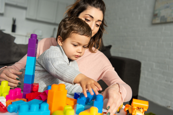 kleine jongen en zijn moeder spelen met kleurrijke kunststof blokken thuis - Foto, afbeelding