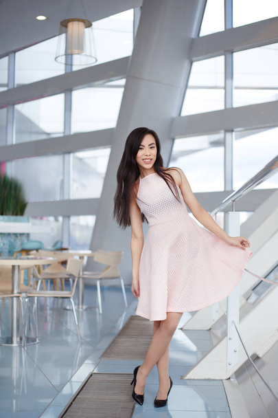 молода усміхнена азіатська жінка в рожевій сукні позує в кафе
 - Фото, зображення