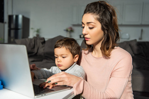 cute little boy and his mother using laptop at table in living room at home - Foto, Bild