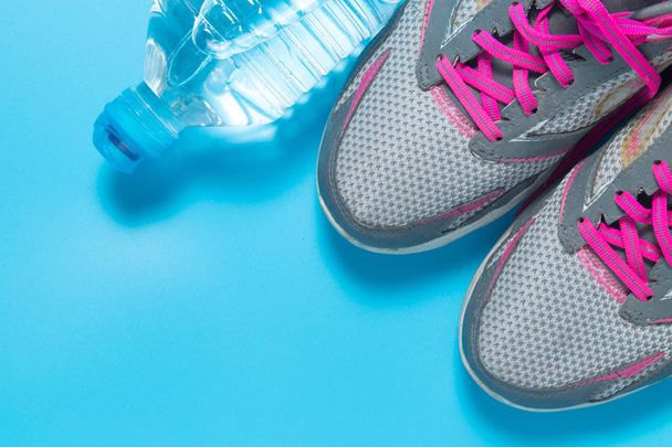 Sport flach legen rosa Schuhe und Flasche Wasser auf blauem Hintergrund mit Copyspace für Ihren Text. Konzept gesunde Lebensweise und Ernährung. - Foto, Bild