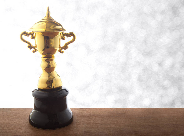 Trofeo dorado sobre mesa de madera sobre fondo bokeh blanco abstacto. Ganar premios con espacio de copia
. - Foto, Imagen