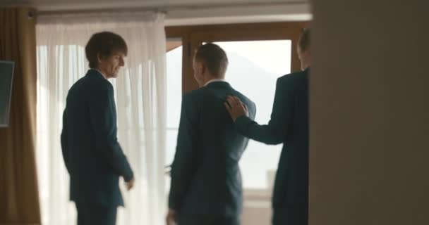 Wedding at Montenegro. Traditional European ceremony. Morning before the reception. 4k. Groomsmen help groom to put on his suit in a hotel room - 映像、動画