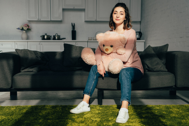 beautiful woman sitting on sofa with pink teddy bear in living room at home - Fotó, kép