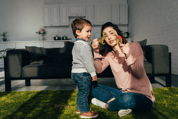 attraente madre mostrando dinosauri giocattolo al suo piccolo figlio in soggiorno a casa
 - Foto, immagini