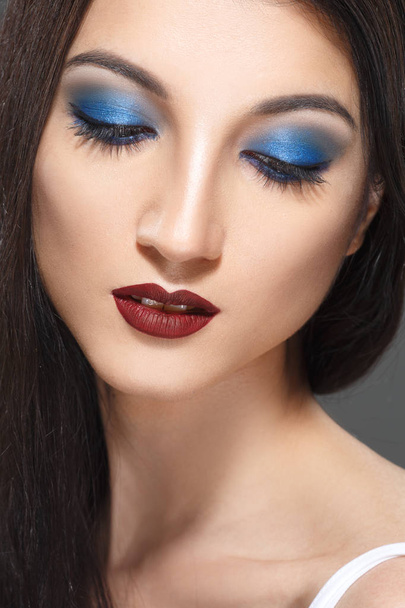 fashion portrait of brunette woman with bright blue eyes makeup on grey backdrop - Foto, imagen