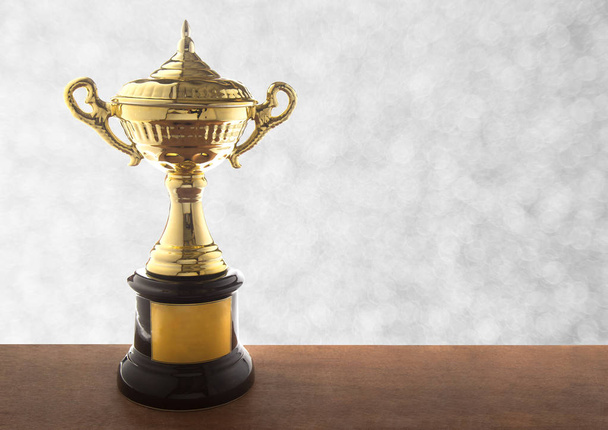 Gouden trofee op houten tafel over abstact bokeh van de witte achtergrond. Winnende awards met kopie ruimte. - Foto, afbeelding