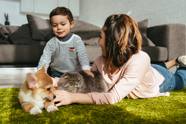 madre e hijo tendidos en el suelo con perro y gato en la sala de estar en casa
 - Foto, imagen