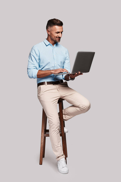 good looking man using laptop in studio and sitting on chair  - Zdjęcie, obraz