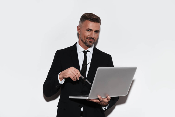 handsome business man with laptop, standing against white background and looking at camera - Valokuva, kuva