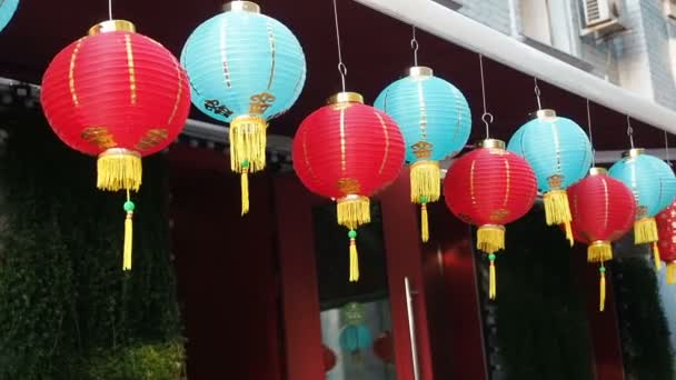Во второй половине дня китайские фонари раскачиваются на ветру. Восточные бумажные огни красного и синего цветов колеблются с ветром на крыше здания днем на улице
 - Кадры, видео