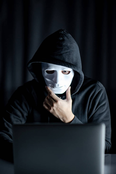 Hacker man met wit masker kijken naar laptop - Foto, afbeelding