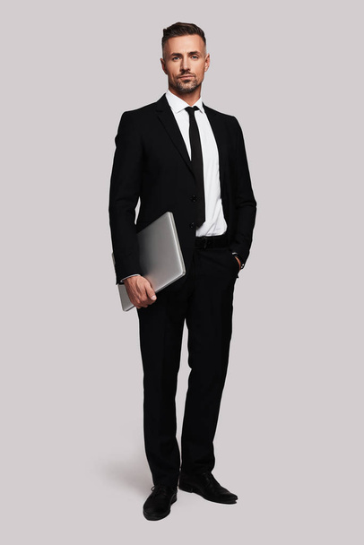 full length of business man holding laptop, standing against white background - 写真・画像