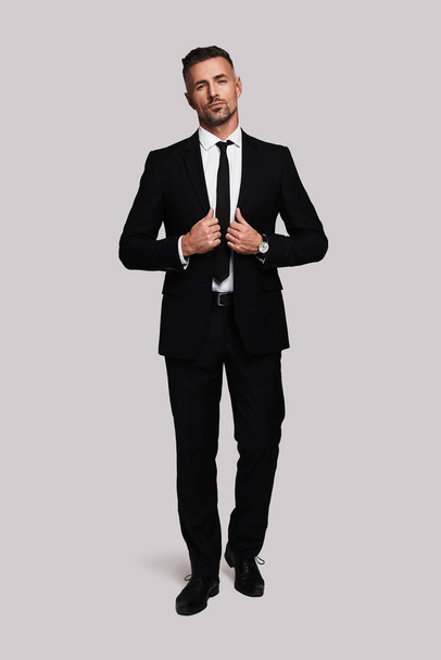 Confident businessman, Full length of handsome man adjusting jacket and looking at camera while standing against grey background - Foto, imagen