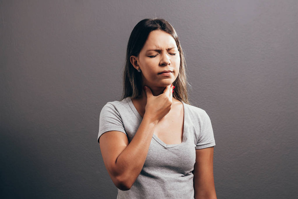 Woman suffering from sore throat over gray background - Foto, Imagem