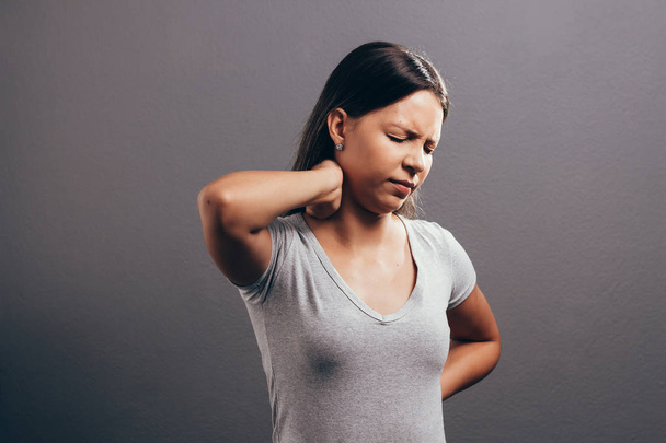 Young woman with neck pain over gray background - Fotoğraf, Görsel