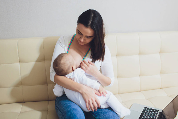 Beautiful young mother working with laptop computer and breastfeeding her newborn baby at home. Mom - business woman. - Foto, Imagem