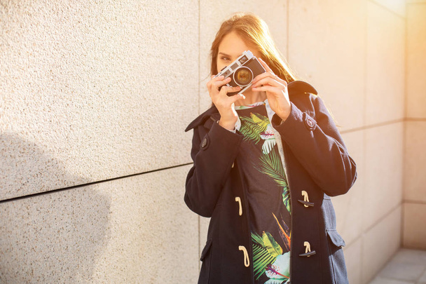 Gelukkig hipster meisje foto met retro camera op stad straat maken. Zon flare - Foto, afbeelding