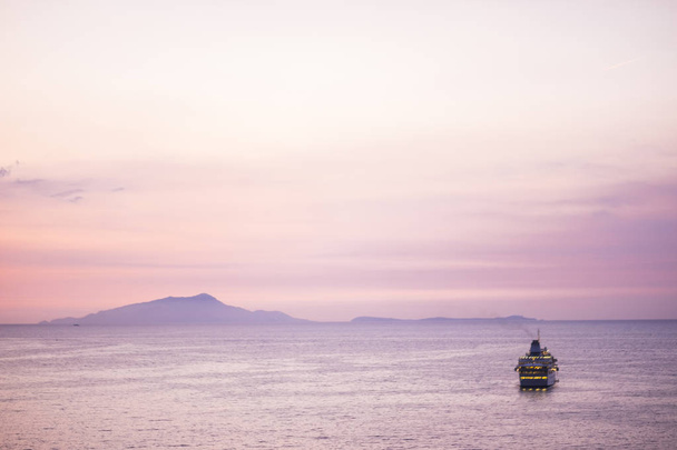 Touristic cruise boat floating in sea on pink colored sunset background - Фото, изображение
