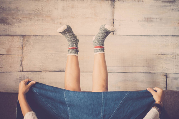 Vistas raras piernas mujer con grandes jeans falda en casa en posición inversa de suelo a arriba con calcetines calientes felices y pared de madera en segundo plano.  - Foto, imagen