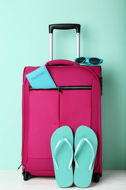 Pink suitcase with flip-flops, passport and sunglasses on wooden table - Фото, зображення