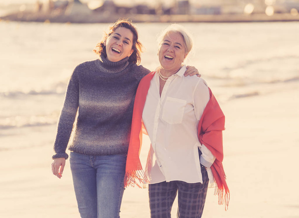 Portrait of happy senior mother and adult daughter spending time together holding hands laughing and walking on beach at sunset light in Happy family moments Generations Retirement and People concept. - Foto, immagini