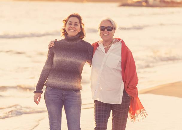 Portrait of happy senior mother and adult daughter spending time together holding hands laughing and walking on beach at sunset light in Happy family moments Generations Retirement and People concept. - Фото, зображення