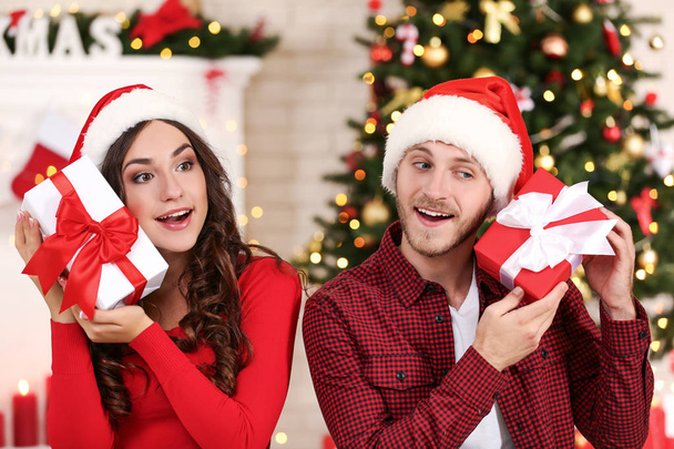 Happy young couple with gift boxes sitting at home near christmas tree - Φωτογραφία, εικόνα