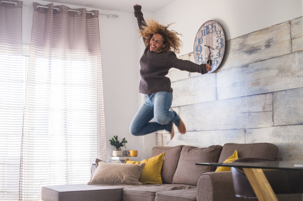Una loca mujer de mediana edad salta a casa sobre el sofá para celebrar el éxito - concepto de gente alegre y feliz.  - Foto, imagen