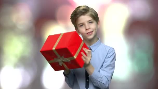 Cute child shaking gift box on blurred background. - Imágenes, Vídeo