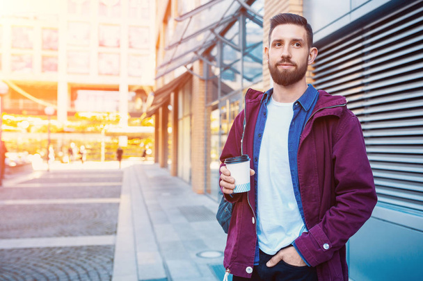 Csinos, fiatal férfi a kávéfogyasztás lila széldzseki. A srác kávét iszik az utcán. Napsütés fáklyát - Fotó, kép
