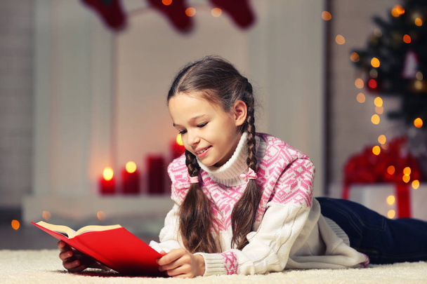 Young girl with red book lying near christmas tree at home - 写真・画像