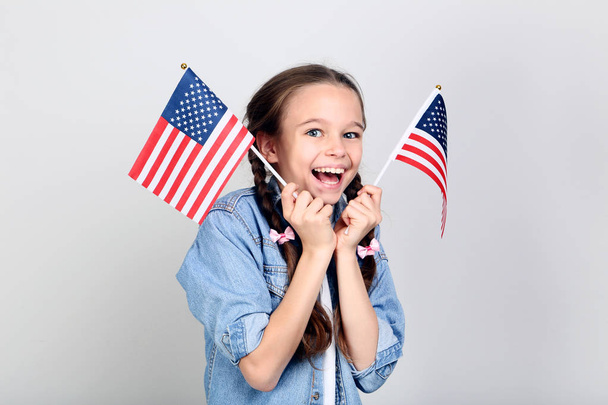 Young girl holding an American flag on grey background - Фото, изображение