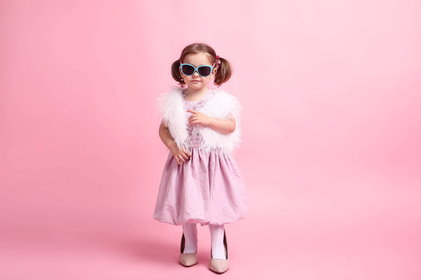 Kaunis pieni tyttö muoti vaatteita vaaleanpunainen tausta
 - Valokuva, kuva