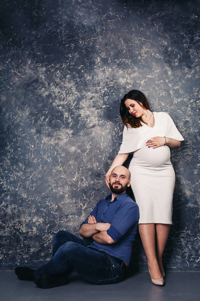 счастливая молодая беременная пара в студии на тёмном фоне. семейные отношения
. - Фото, изображение